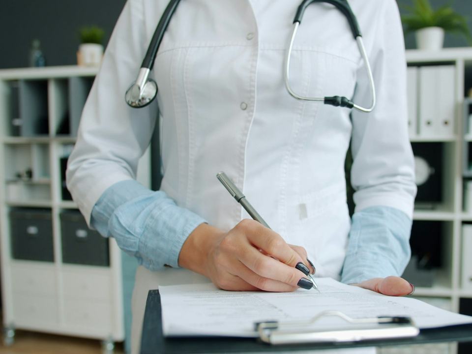 Un médecin prend des notes à la main sur un porte-bloc